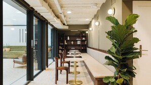 A modern interior with a long bench seating area, tables, and a large potted plant. - Atipico Madrid (Madrid)