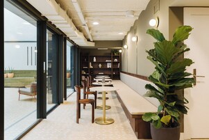 Un intérieur moderne avec un long banc servant de coin salon, des tables et une grande plante en pot.