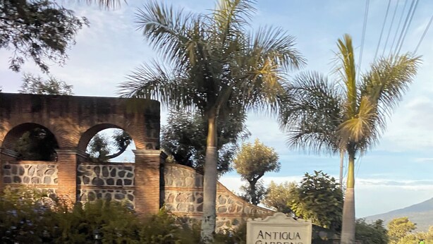 Una entrada empedrada a Antigua Gardens, con un muro de piedra y palmeras.