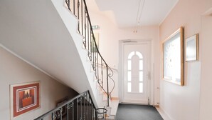 Una escalera con barandilla de metal, una puerta con un ventanal arqueado y cuadros en las paredes.