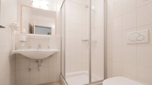 Un baño moderno con lavamanos, espejo, ducha e inodoro.