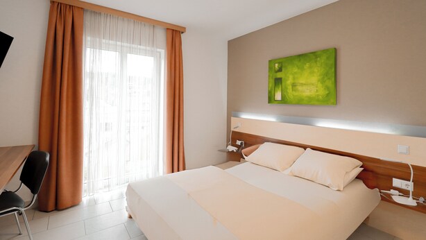 Una habitación de hotel con cama, escritorio y ventana con cortinas.