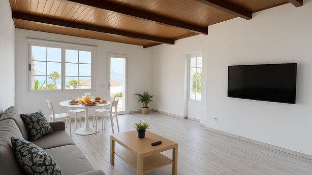 A spacious living room with a wooden ceiling, a flat-screen TV mounted on the wall, a grey sofa with patterned cushions, a wooden coffee table, and a dining area with a table and chairs. - Charming Rural House (Arona)