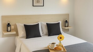 A neatly made bed with a white and gray bedspread, black and white pillows, a framed artwork above the headboard, and a tray with a croissant, coffee cup, and a flower on the bed. - Charming Rural House (Arona)