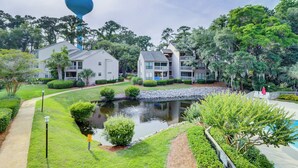 A residential area with two-story houses, a small pond, and a walking path. - Sunset Rentals | Lighthouse Tennis 2387 (Hilton Head Island)