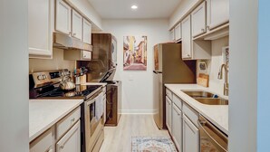 A narrow kitchen with white cabinets, stainless steel appliances, and a tiled backsplash. - Sunset Rentals | Lighthouse Tennis 2387 (Hilton Head Island)