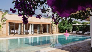 En swimmingpool med en pink flyder, omgivet af liggestole og en bygning med store vinduer.