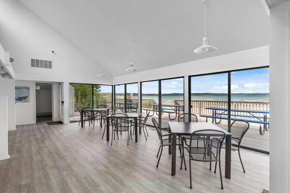 A spacious indoor dining area with large windows overlooking a beach, featuring modern furniture and a wooden floor.