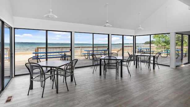 A spacious dining area with large windows overlooking a beach, featuring wooden flooring and modern furniture. - Peaceful 3-Bedroom Retreat with Lake Michigan Views & Access (Harbor Springs)
