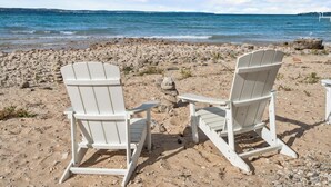 Two white Adirondack chairs facing a rocky beach with a view of the ocean and distant land. - Peaceful 3-Bedroom Retreat with Lake Michigan Views & Access (Harbor Springs)