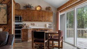 A kitchen with wooden cabinets, a dining table with chairs, and a large window with a view of trees. - Peaceful 3-Bedroom Retreat with Lake Michigan Views & Access (Harbor Springs)