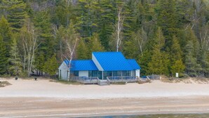 A two-story building with a blue roof, situated on a sandy beach with a forested backdrop. - Peaceful 3-Bedroom Retreat with Lake Michigan Views & Access (Harbor Springs)