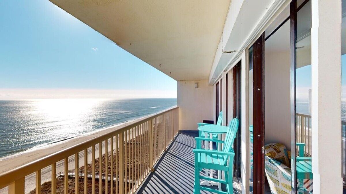 Ein Balkon mit Blick auf das Meer, einem Geländer und zwei türkisfarbenen Stühlen.