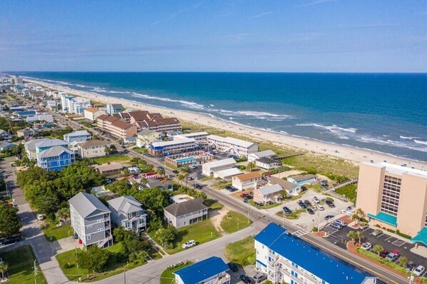 An aerial view of a coastal town with a beachfront, buildings, and a road leading to the beach.