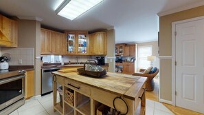 A kitchen with wooden cabinets, a central island, and a dining area with a wicker chair.