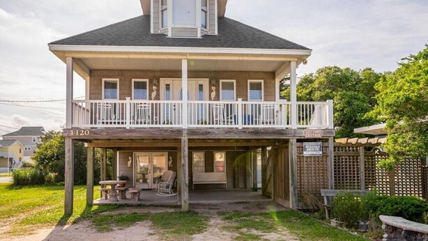 Une maison à deux étages dotée d’un balcon, d’un porche avant couvert et d’une enseigne indiquant « Cotton’s Cottages ».