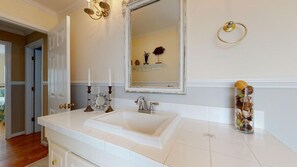 Un baño con un lavabo grande de color blanco, un espejo y un jarrón decorativo en la encimera.