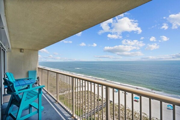A balcony with a view of the ocean, a beach, and a clear sky.