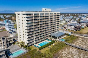 A high-rise hotel with multiple balconies, a swimming pool, and a beach view.