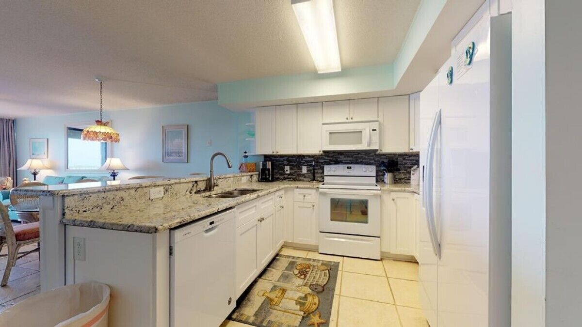 Una cocina compacta con armarios blancos, un microondas y una estufa. Hay una pequeña isla con un lavamanos y una alfombra decorativa.