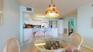 Un coin repas avec une table en verre, des chaises en osier et un luminaire décoratif suspendu.
