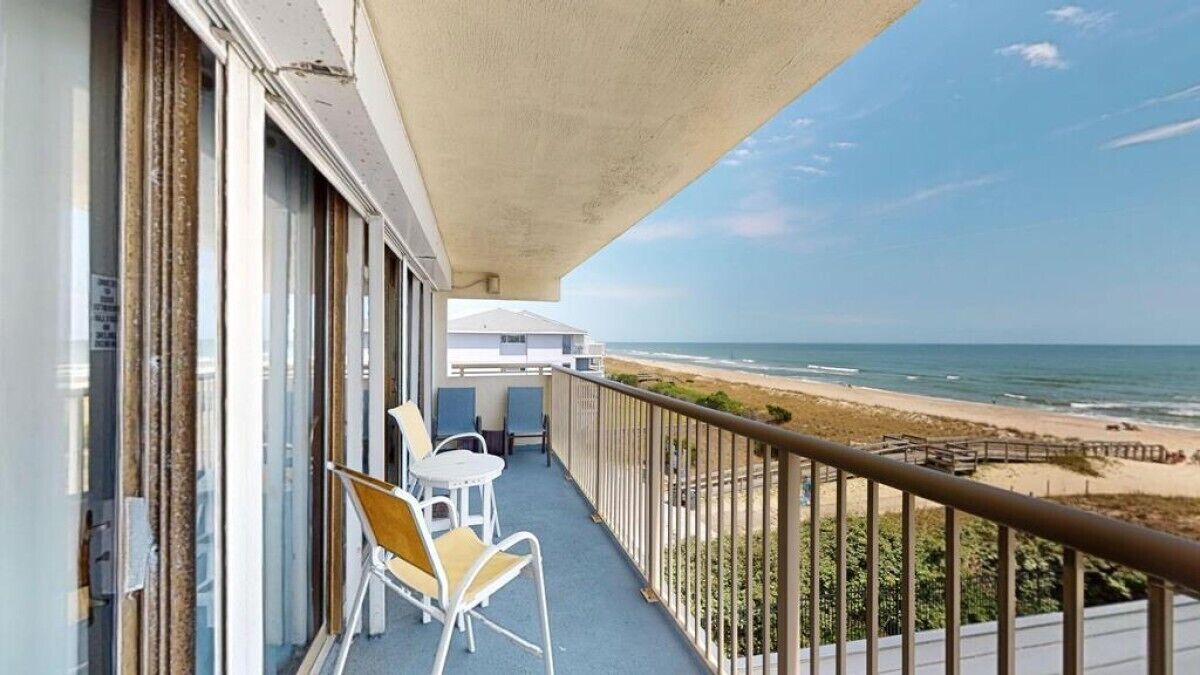 Een balkon met uitzicht op het strand, een leuning en twee stoelen.