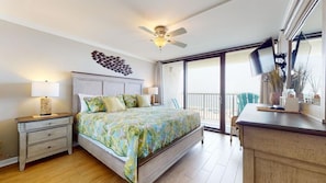 A bedroom with a bed, nightstand, lamp, ceiling fan, and a view of the balcony.