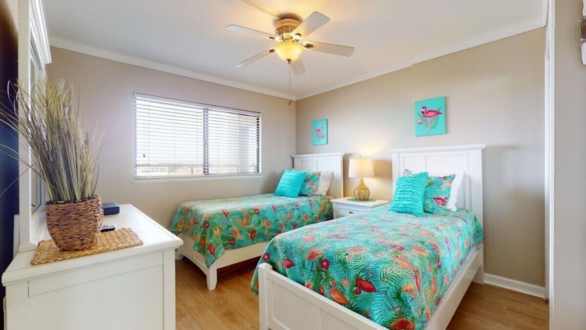 A bedroom with two beds, a ceiling fan, a window with blinds, and a wall-mounted lamp.