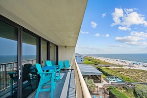 A balcony with turquoise chairs and a view of the beach and ocean.