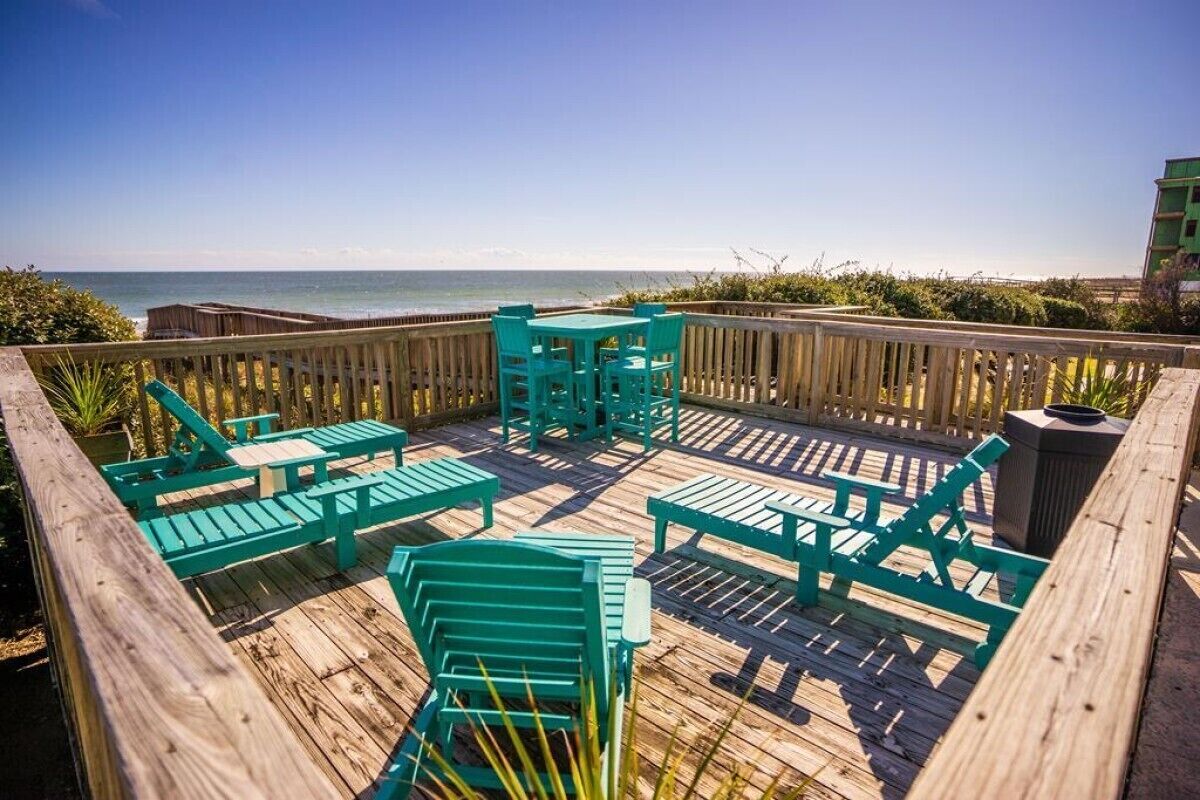 A wooden deck with turquoise chairs and tables overlooking the ocean.