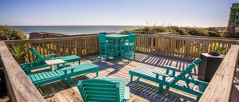 A wooden deck with turquoise chairs and tables overlooking the ocean.