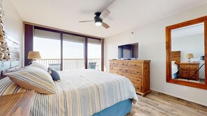 Une chambre à coucher comprenant un lit, une commode en bois, un téléviseur et un grand miroir.