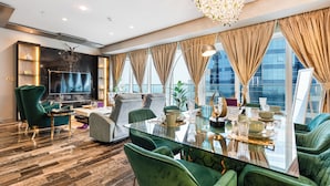 A modern living room with a glass dining table, green upholstered chairs, a large flat-screen TV, and a chandelier. - High End Luxury Stay with Full Palm Jumeirah View (Dubai)