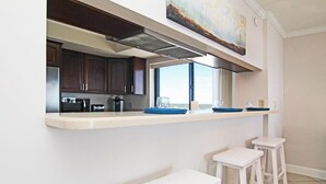 Una cocina con armarios de madera oscura, un refrigerador de acero inoxidable, un microondas y una cafetera. Hay una ventana sobre el mostrador y un cuadro en la pared.