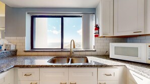 A modern kitchen with a large window, granite countertops, white cabinetry, and a built-in microwave. - Pelican Watch 907-Lovely end unit with views galore and elevators (Carolina Beach)