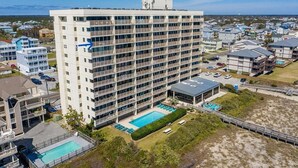 A multi-story hotel with a pool area, surrounded by other buildings. - Pelican Watch 907-Lovely end unit with views galore and elevators (Carolina Beach)