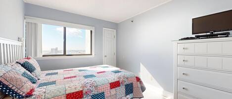 Een slaapkamer met een bed, een dressoir, een televisie en een raam met uitzicht op de stad.