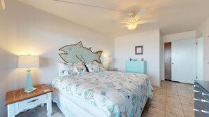 Quarto com uma cama, duas mesas de cabeceira, um ventilador de teto, cômoda e uma porta.