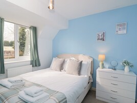 Un dormitorio con una cama, un tocador, una ventana con cortinas y una pared con dos cuadros.