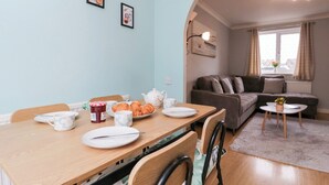 A dining area with a table set for two, a sofa, and a small coffee table. - 20 Honeycroft (Cheltenham)