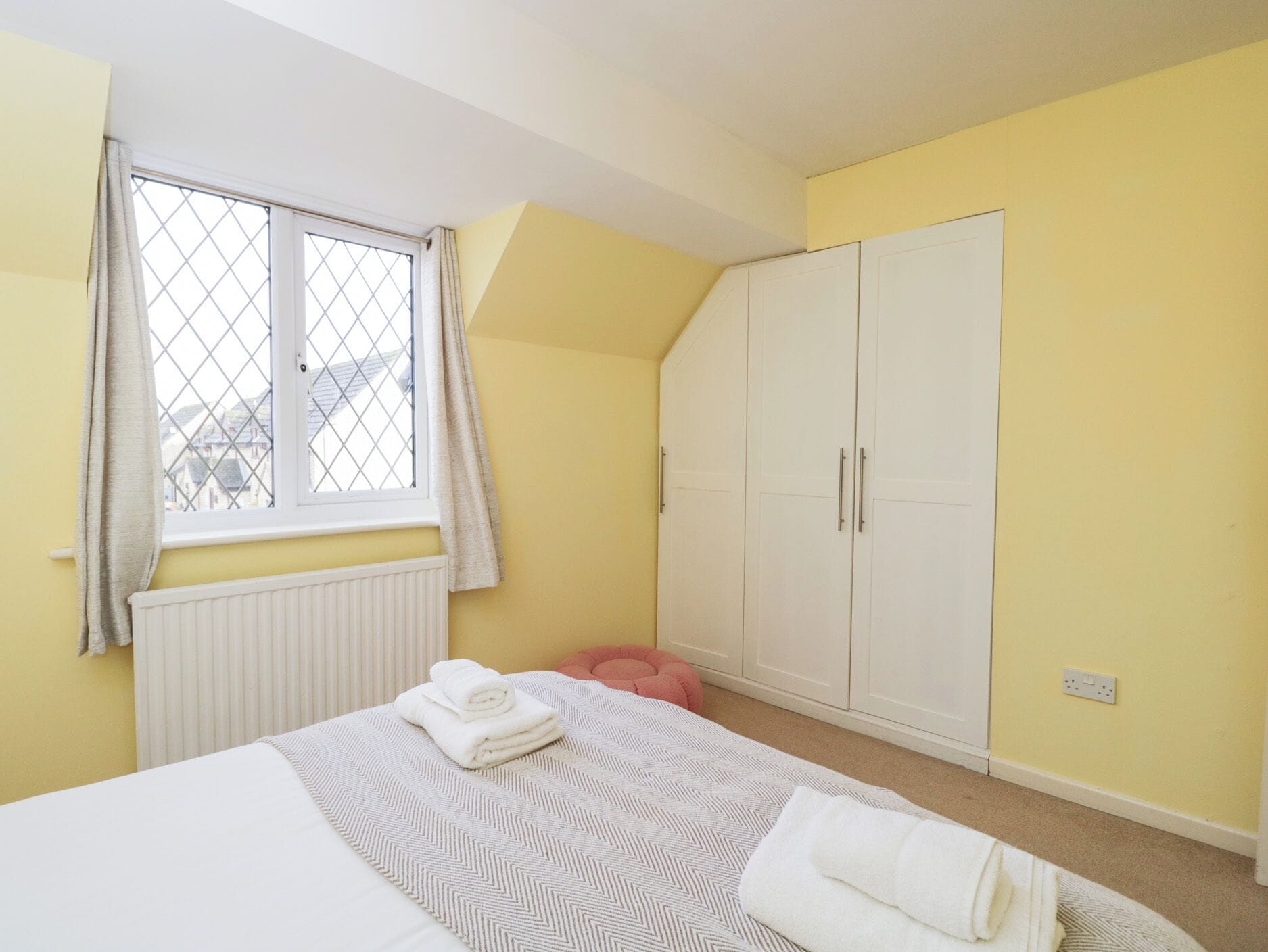 Ein Schlafzimmer mit einem Bett, einem Fenster mit Vorhängen, einem Kleiderschrank und einer Heizung.