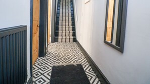A narrow hallway with patterned flooring, a wooden door, and a staircase with striped carpet.