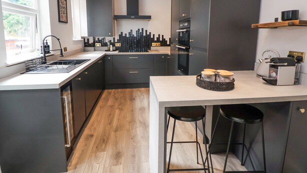 A modern kitchen with dark cabinetry, a central island, and a built-in oven.