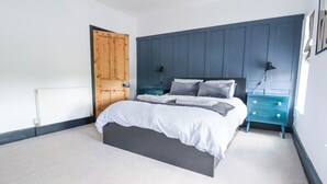 A bedroom with a bed, a wooden door, a blue nightstand, and a white radiator.
