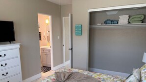 Une chambre à coucher avec un lit, une commode, un téléviseur et une salle de bain visible à travers une porte ouverte.