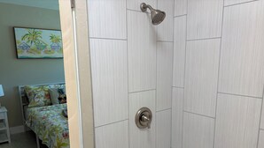 Une salle de bain avec une douche, une baignoire et une porte donnant sur une chambre à coucher équipée d’un lit et d’une table de chevet.