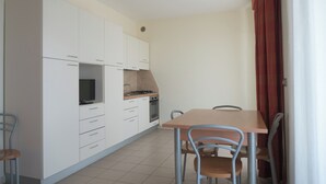 Una cocina compacta con armarios blancos, estufa y una mesa de comedor con sillas.
