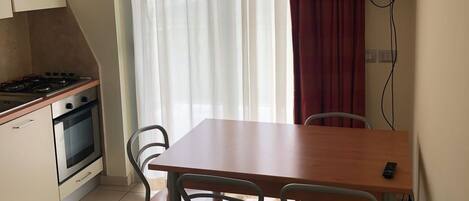 A compact kitchen with a gas stove, oven, and a dining table with four chairs. A TV is mounted on the wall above the table.