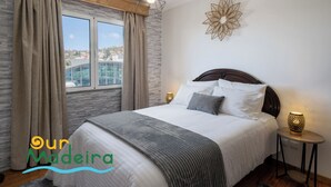 Un dormitorio con una cama grande, una ventana con cortinas, un adorno en la pared y lámparas de noche.