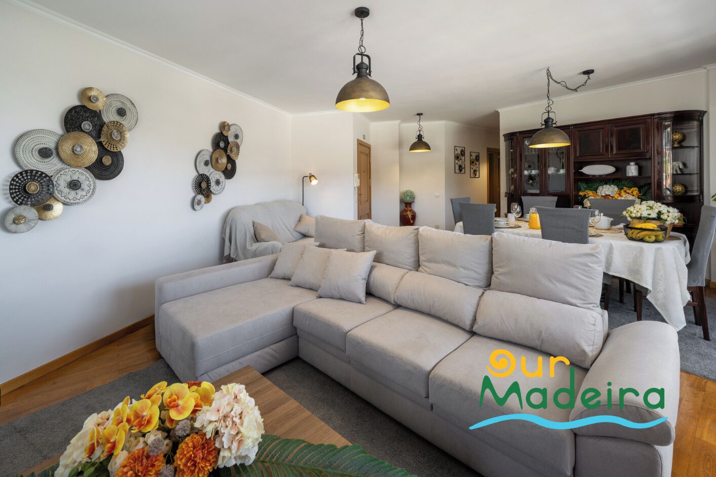 Una sala de estar moderna con un sofá modular, arte decorativo en la pared y un comedor con una mesa dispuesta para dos.